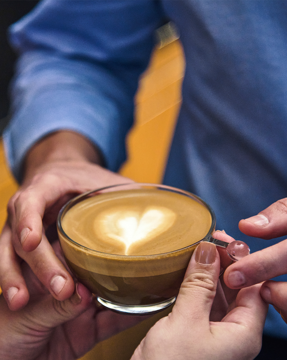 Mãos trocando uma xícara de café com desenho de coração